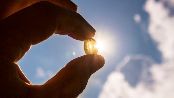 Pessoa segurando cápsula de vitamina D na direção do Sol