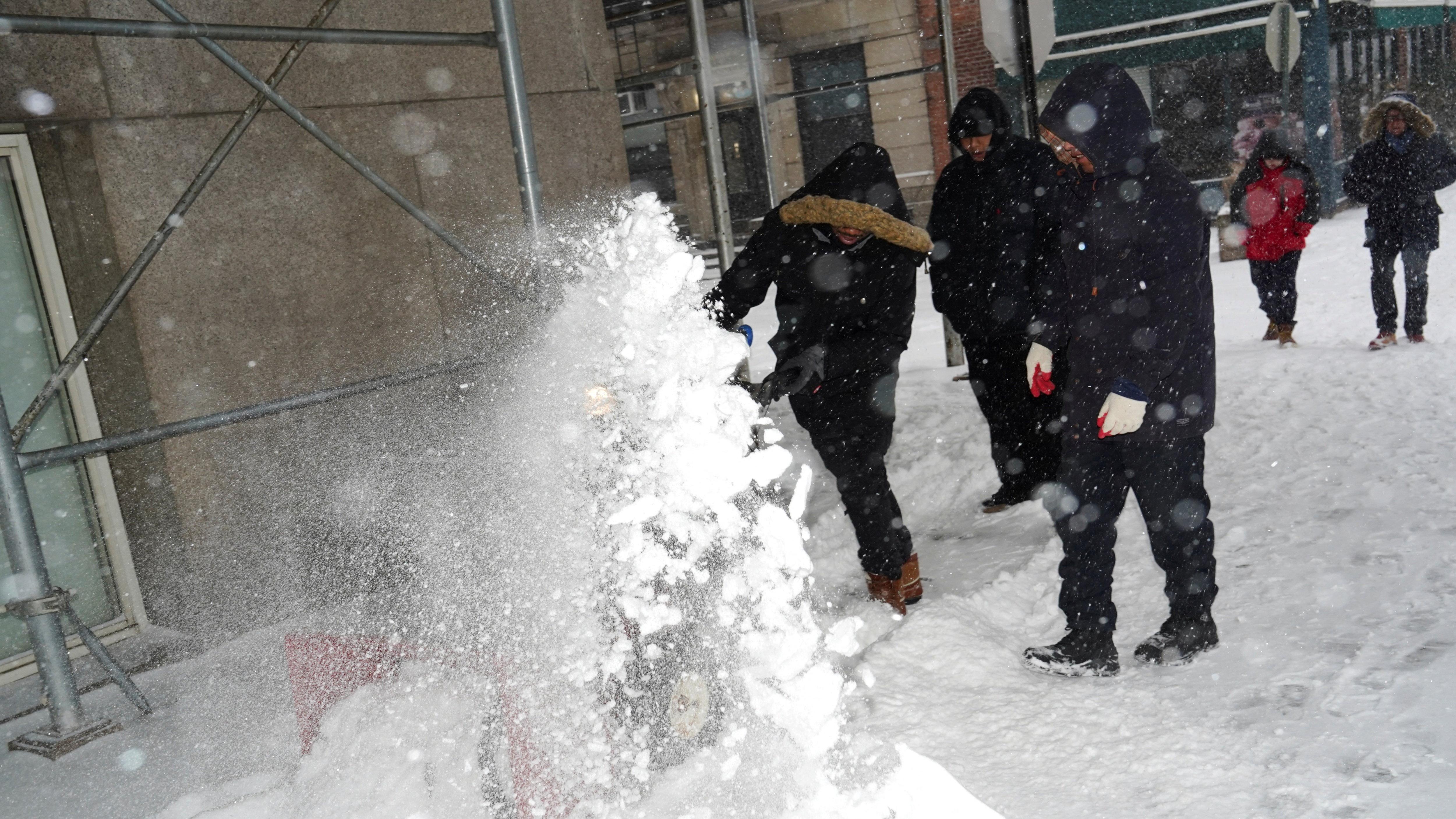 عمال يرتدون سترة سوداء وسروالاً أسود، وقفازات ويغطون رؤوسهم بعظاء رأس واقٍ من البرد، بينما يستخدمون آلات لإزالة الثلج من رصيف المشاة بينما تمتد العاصفة الشتوية "فيرن" عبر مساحة واسعة من الولايات المتحدة، في بروكلين بمدينة نيويورك في الولايات المتحدة الأمريكية.


