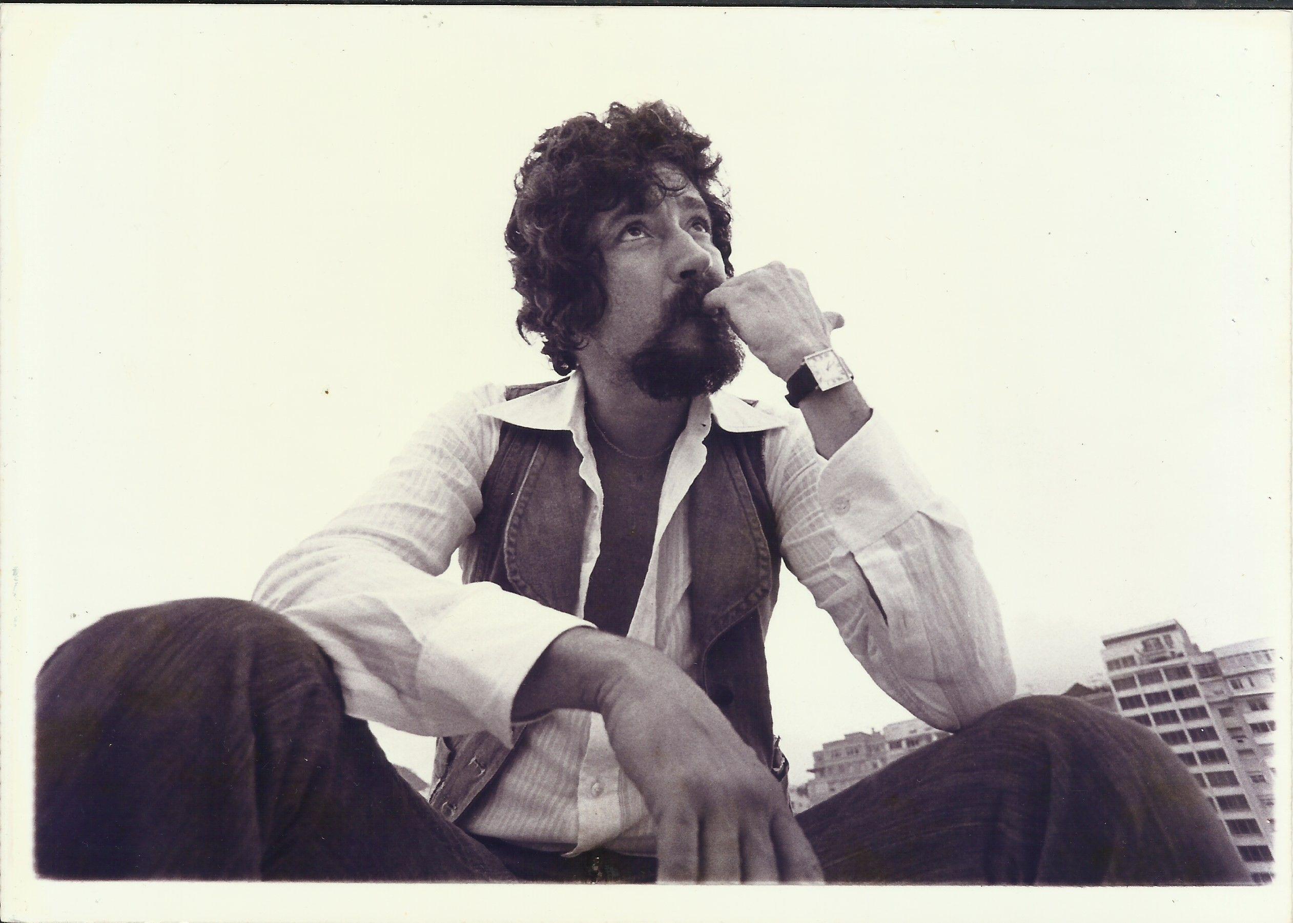 Raul sentado, observando algo e com a mão na boca, como se estivesse preocupado ou compenetrado