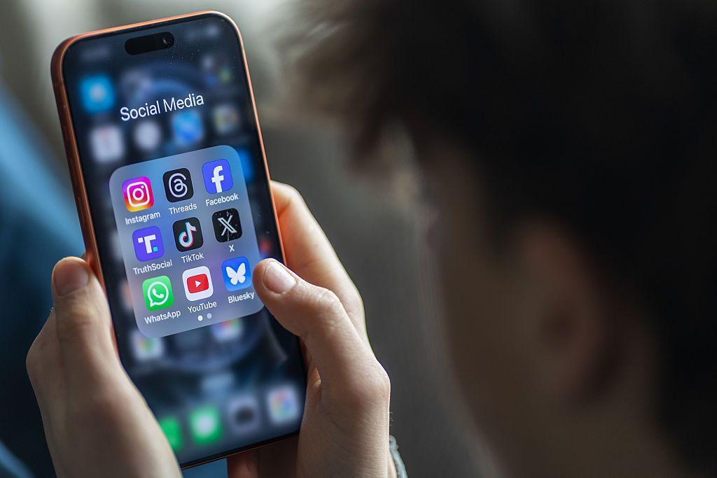 En esta fotoilustración, un joven de 14 años sostiene la pantalla de un iPhone que muestra diversas aplicaciones de redes sociales y mensajería.