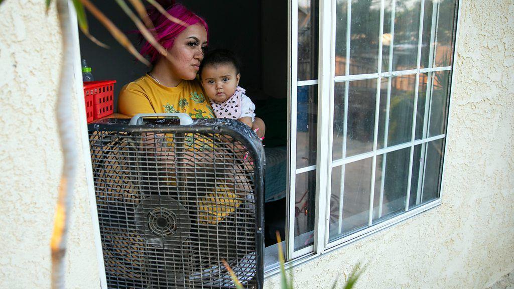 Mulher com criança no colo e um ventilador ligado na sua janela