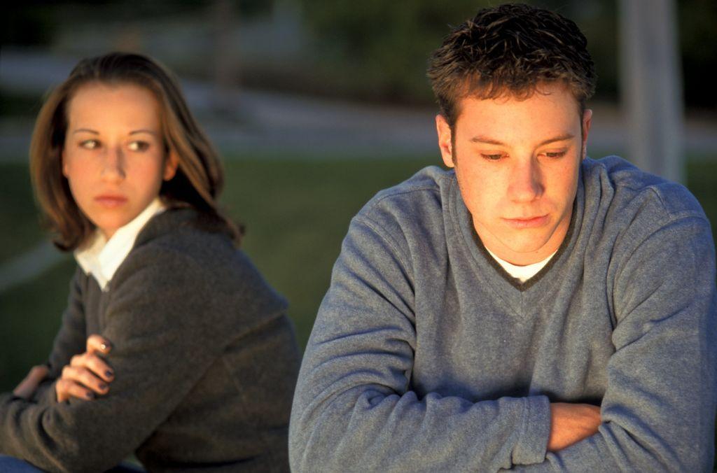 شاب يجلس حزيناً معرضاً عن فتاة تجلس بجواره وتنظر إليه في حزن
