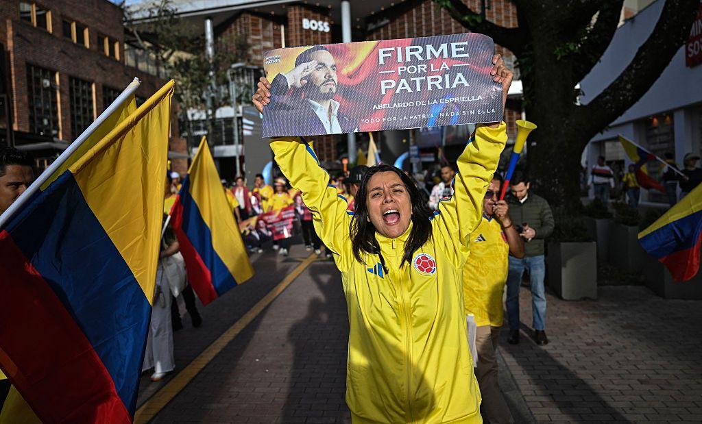 Una mujer vestida con ropa de la selección de fútbol colombiana sostiene un cartel de la campaña de Abelardo de la Espriella con su imagen y el eslógan "Firme por la patria" en Bogotá el 12 de junio de 2026.