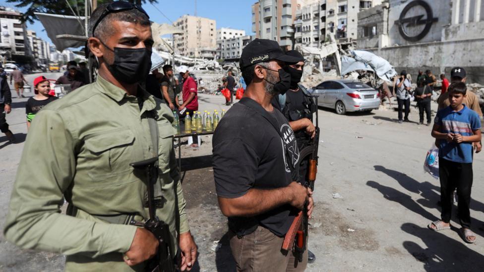 Tres militantes de Hamas con máscaras y armas automáticas hacen guardia en una calle destruida en el centro de Gaza.