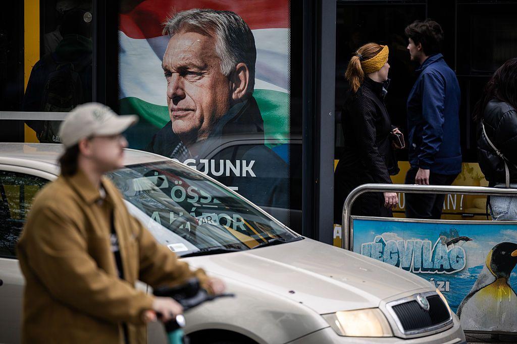 Una calle de Budapest con un auto y una persona en bicicleta y un cartel con el rostro de Viktor Orban. 