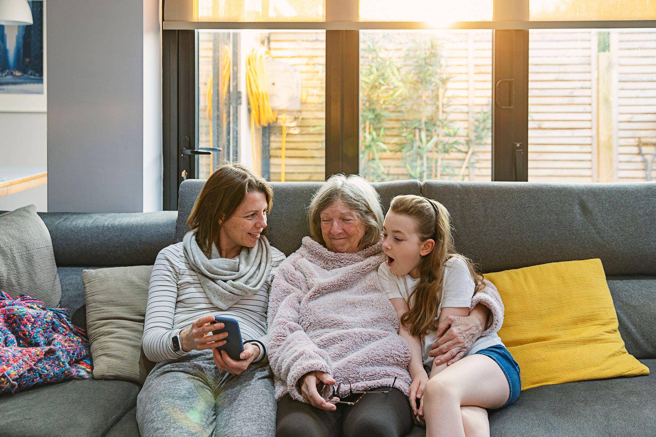 Tres generaciones de mujeres de una misma familia sentadas en un sofá, mirando una foto en un celular