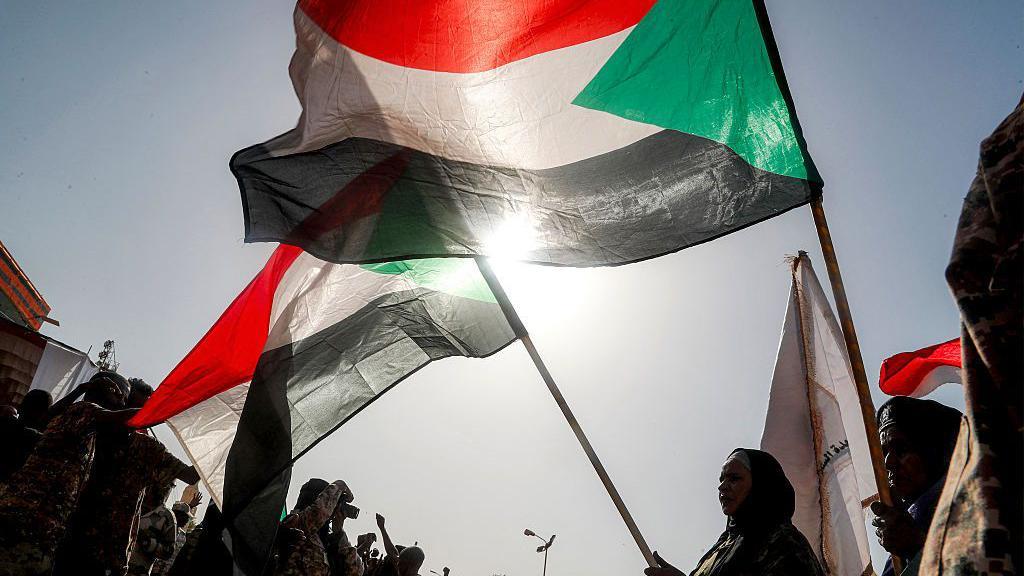 أشخاص يحملون أعلام السودان بينهم سيدة