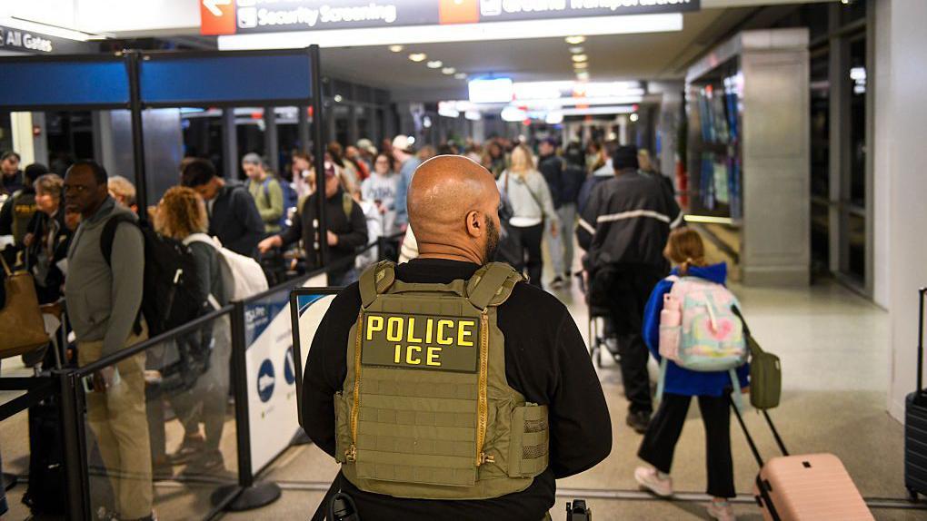 Un agente del ICE está junto a una larga fila de viajeros que esperan pasar por un control de la TSA en el Aeropuerto Internacional de Filadelfia el 28 de marzo de 2026 en Filadelfia, Pensilvania.  (Foto de Matthew Hatcher/Getty Images)