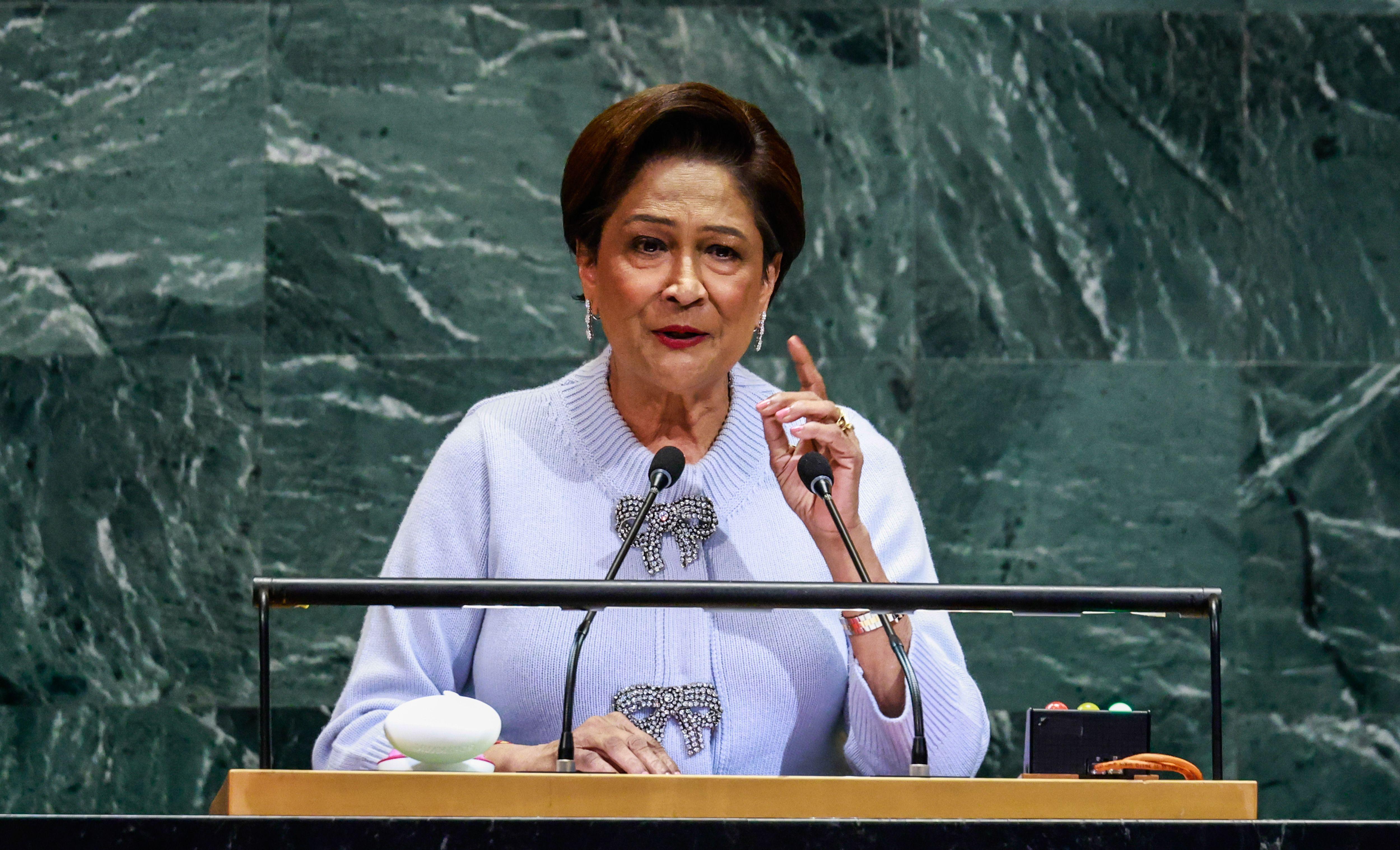 La primera ministra de Trinidad y Tobago, Kamla Persad-Bissessar, está parada en un podio y levanta una mano mientras habla.