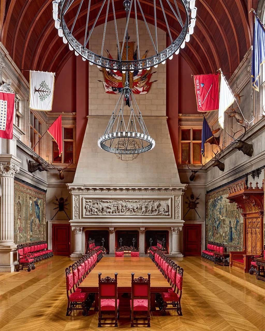 Sala de techos altos y tapices en las paredes. En el centro se ve una larga mesa de madera para banquetes con sillas tapizadas en rojo para cerca de 20 comensales.