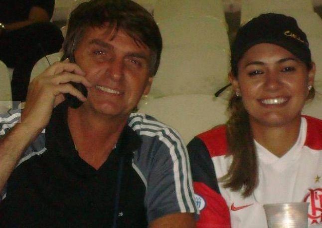 Bolsonaro e Michelle em foto antiga. Ele veste preto e segura um celular pr&oacute;ximo ao ouvido. Ela usa um bon&eacute; preto e veste uma camisa do Flamengo