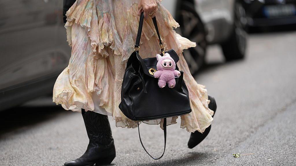 Una muñeca Labubu rosa sujeta a un bolso negro, llevada por una mujer