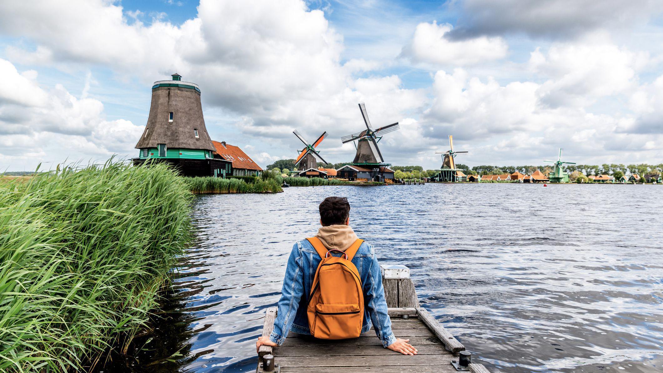 Hombre sentado en el muelle mirando los molinos de viento en Zaanse Schans, Zaandam, Países Bajos.