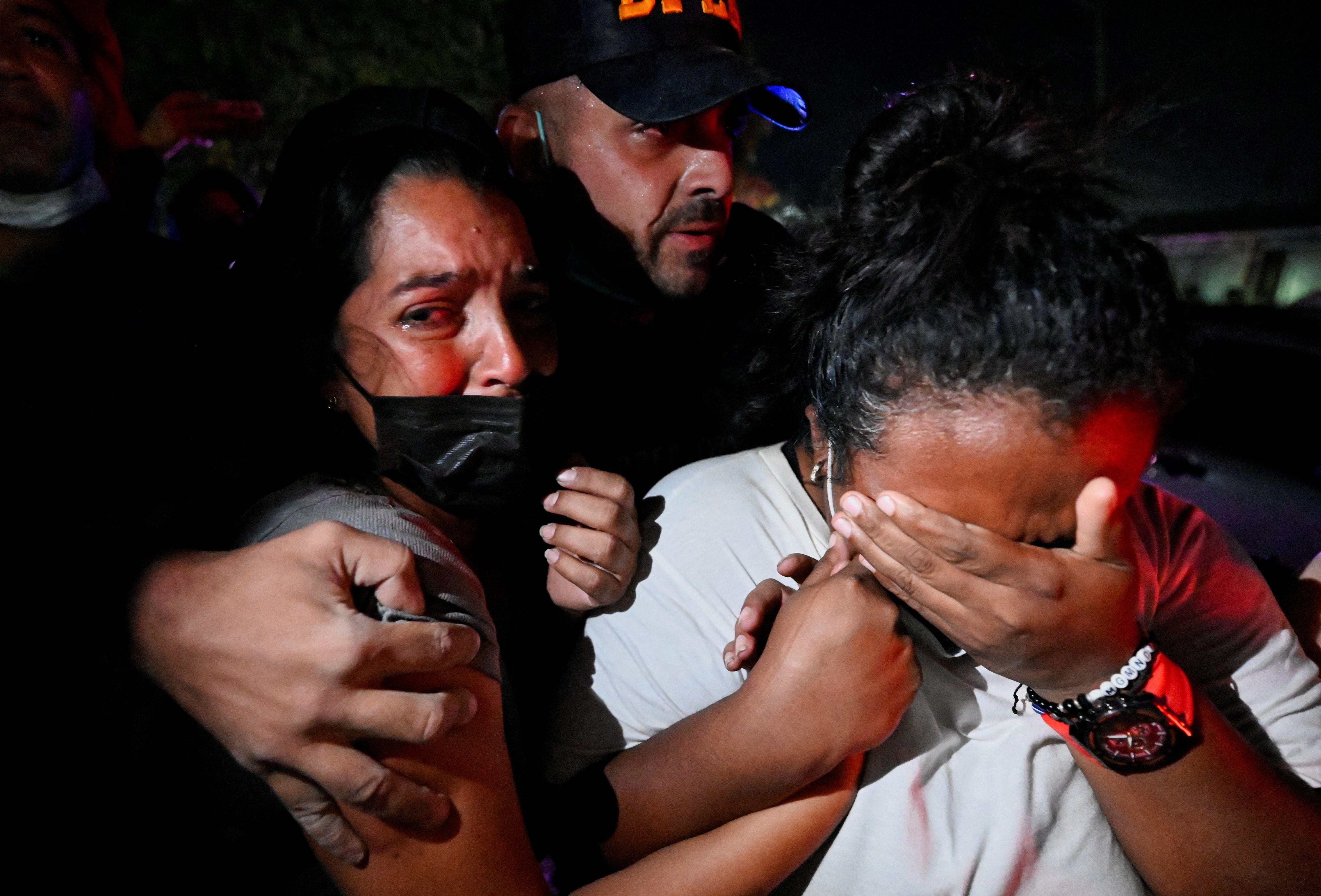 Un hombre abraza a dos mujeres que están desconsoladas llorando mientras intenta sacarlas de donde están.