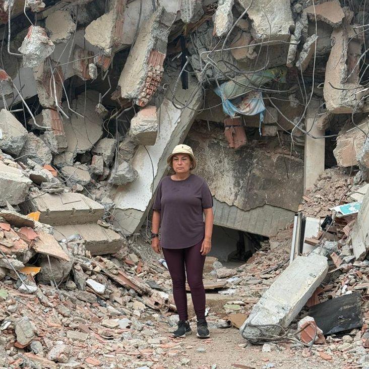 María Lourdes Pérez, vestida com calça e camisa marrom e gorro bege, em frente a uma montanha de escombros, cimento, pedras e partes de uma edificação