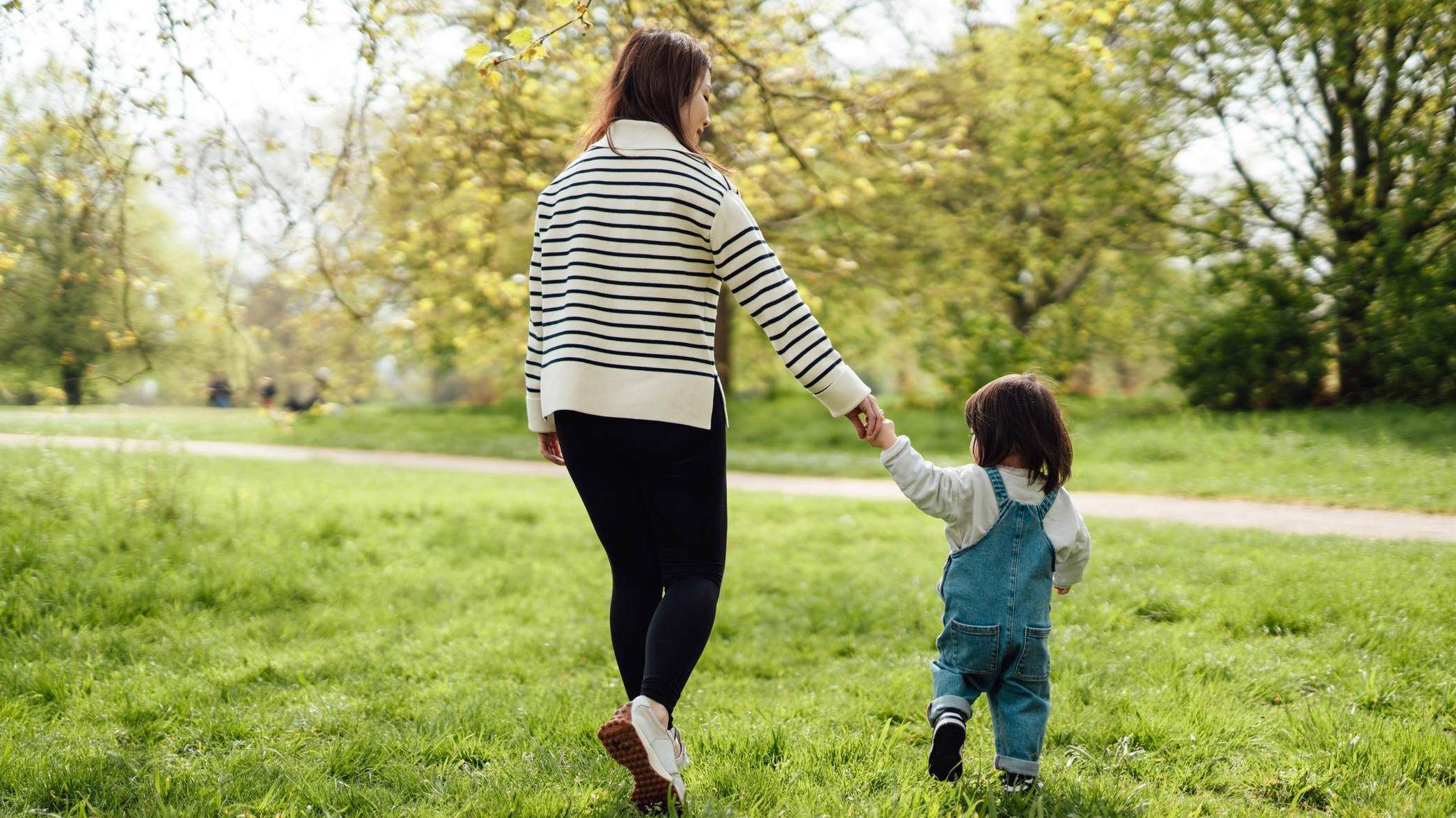 Mulher de costas leva seu filho pela mão para um parque