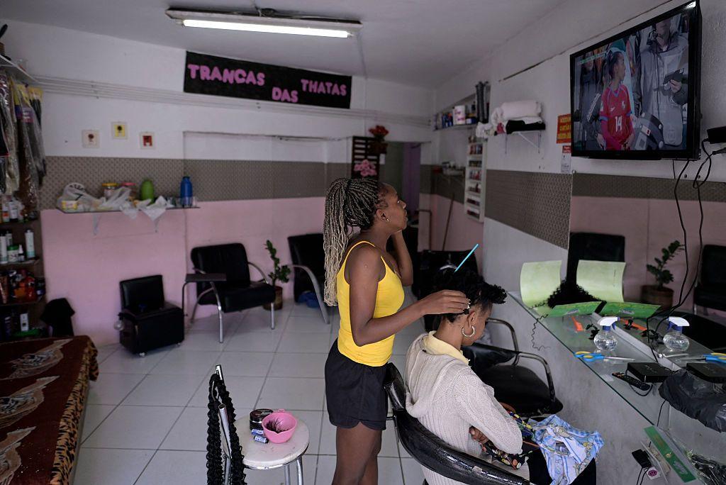 Uma cabeleireira atende uma cliente enquanto assiste um jogo de futebol na televis&atilde;o