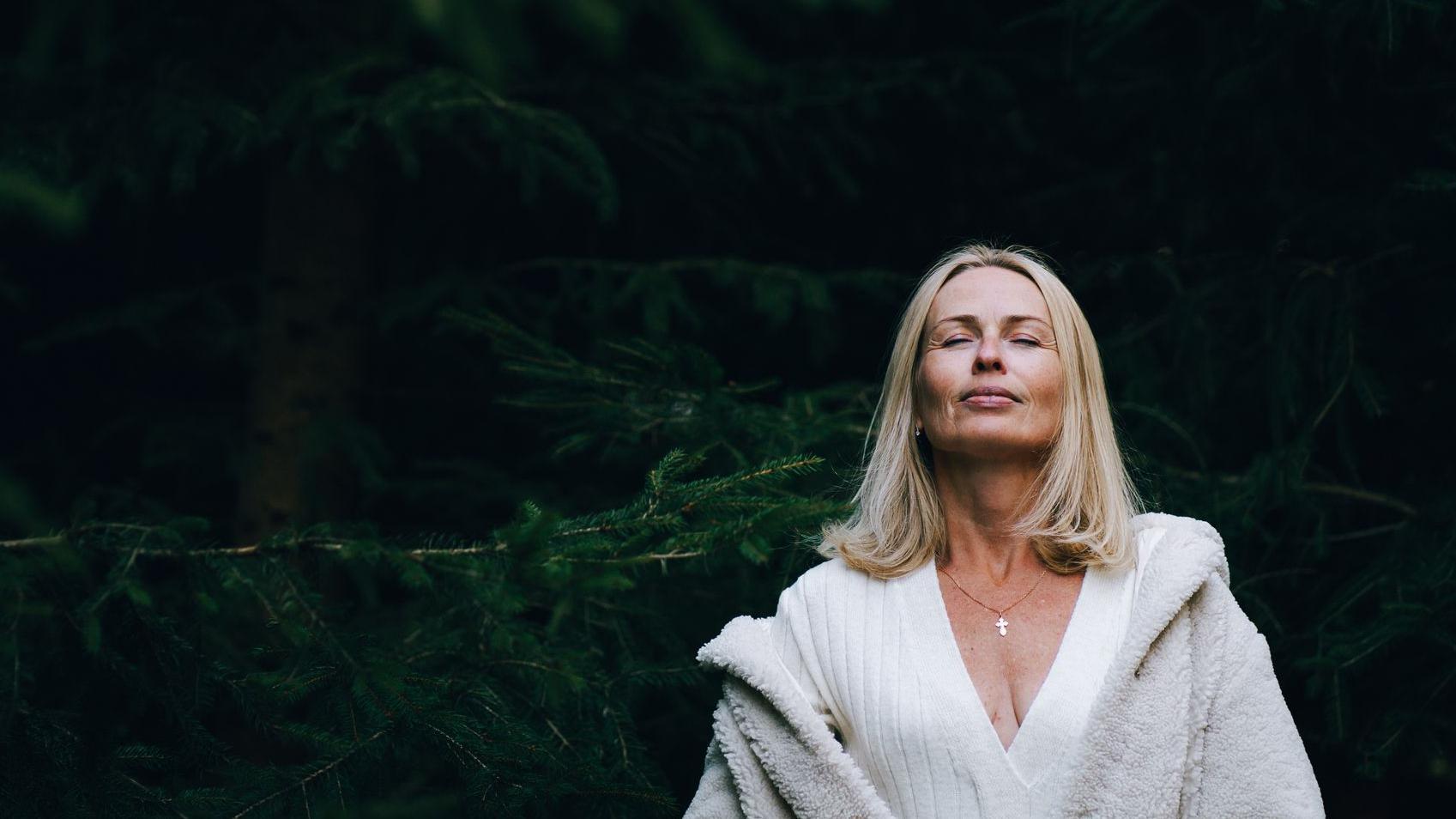 Meditación en un bosque de hoja perenne. Mujer madura paseando por un bosque de coníferas