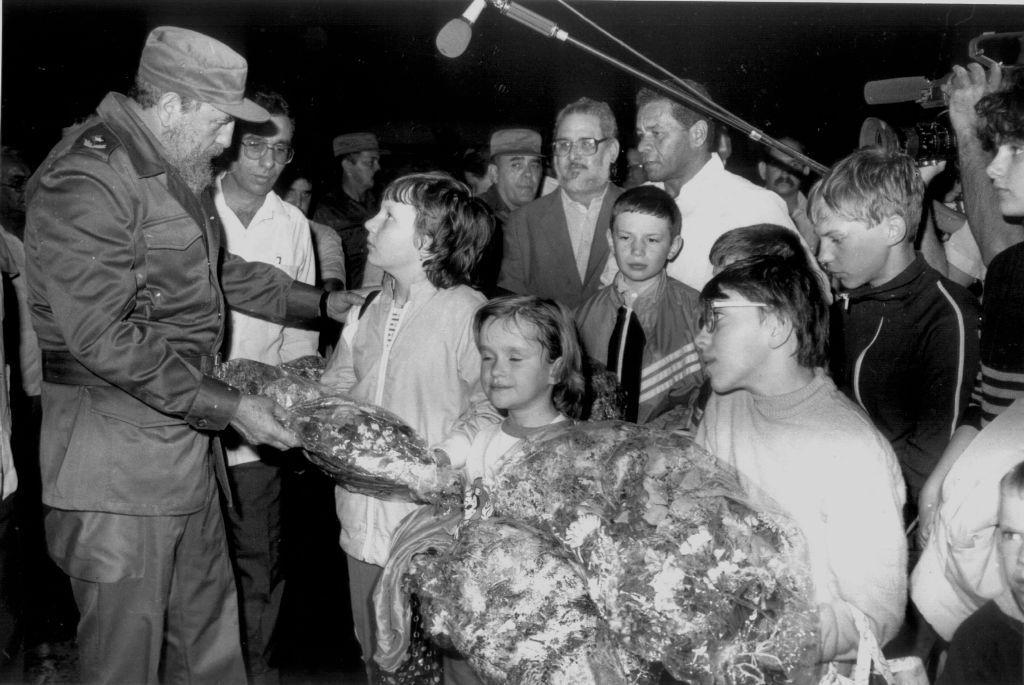 Fidel Castro, en un típico vestido militar verde oliva, le entrega coronas de flores a un grupo de niños que lo miran.