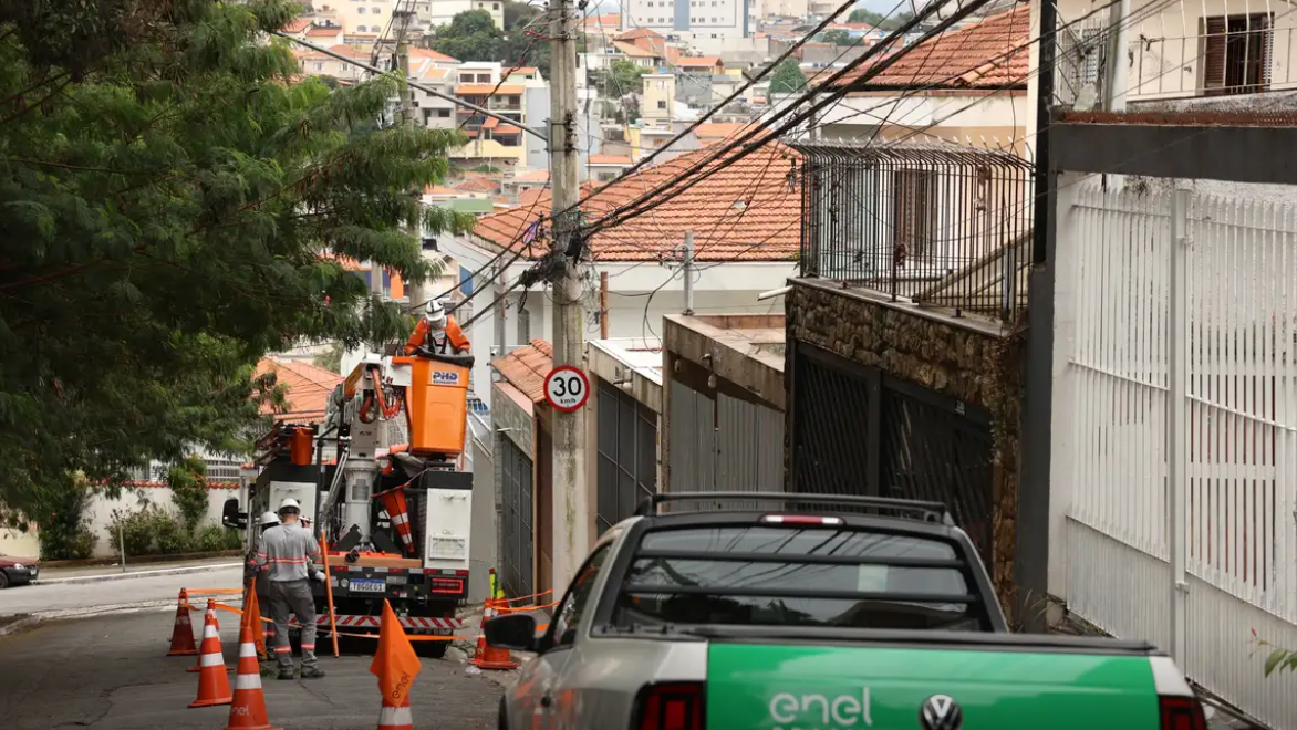Carro da Enel, agência de energia, e funcionários da empresa, em frente a um poste de energia