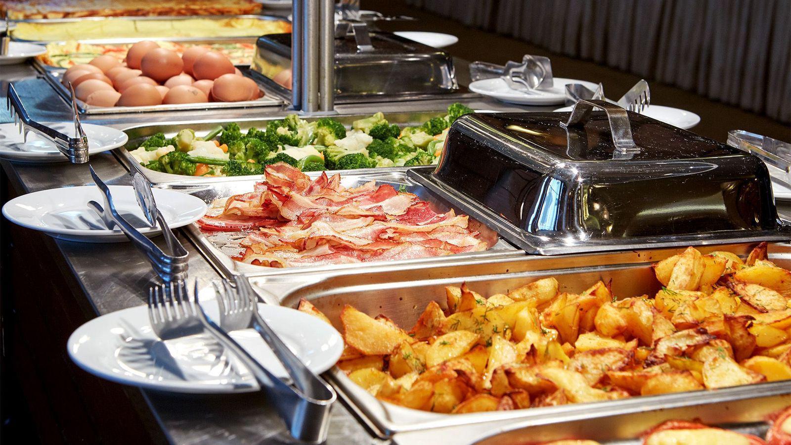 Bandejas de desayuno buffet con papas al horno, tocino, brócoli, huevos y otros platillos.