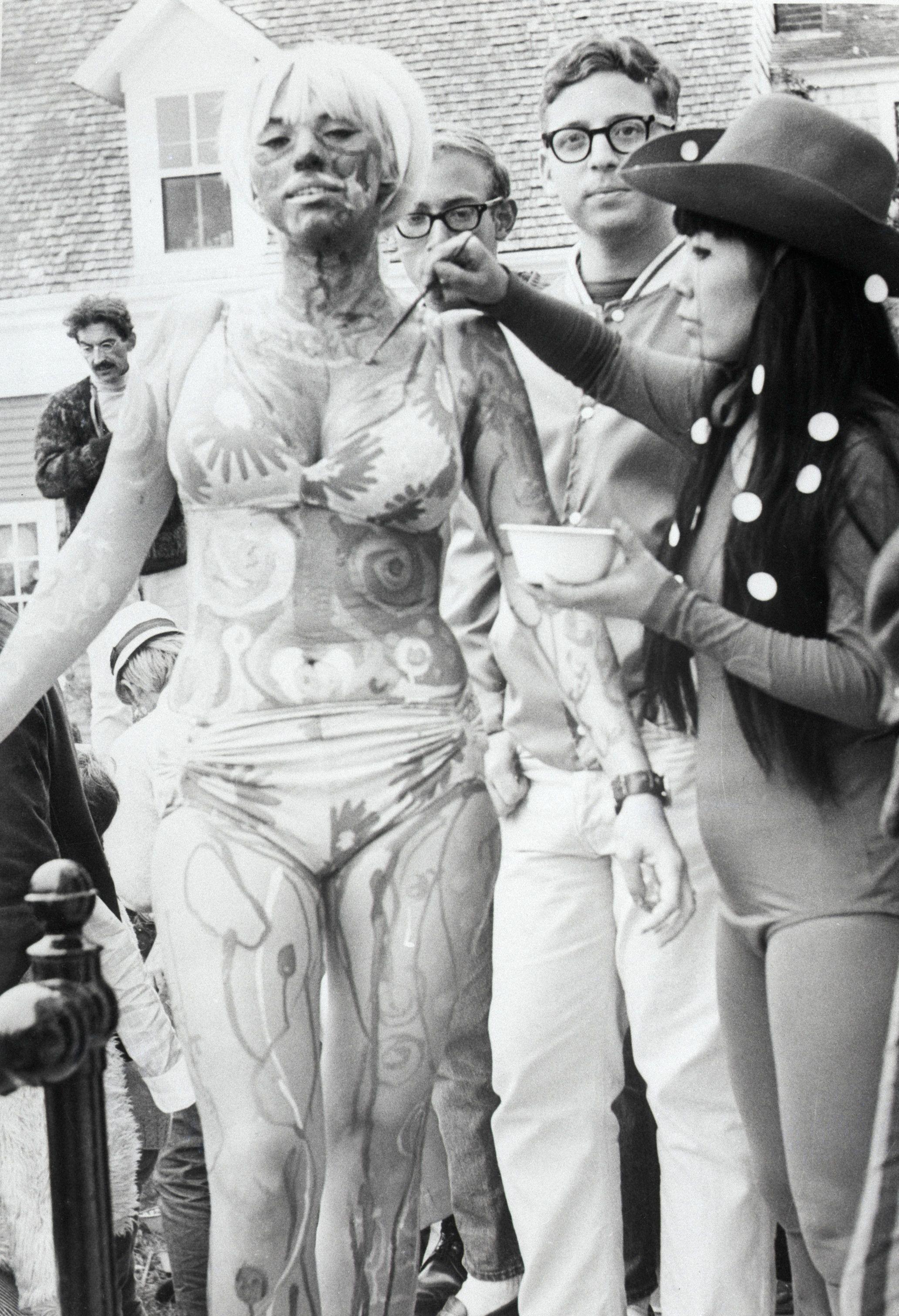Fotografía en blanco y negro de Yayoi Kusama en 1967 pintando a una joven en bikini en un festival de arte corporal en Provincetown, Massachusetts.