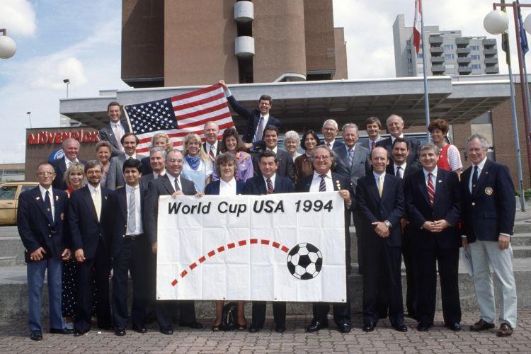 Grupo de pessoas perfiladas exibe a bandeira da Copa do Mundo de 1994