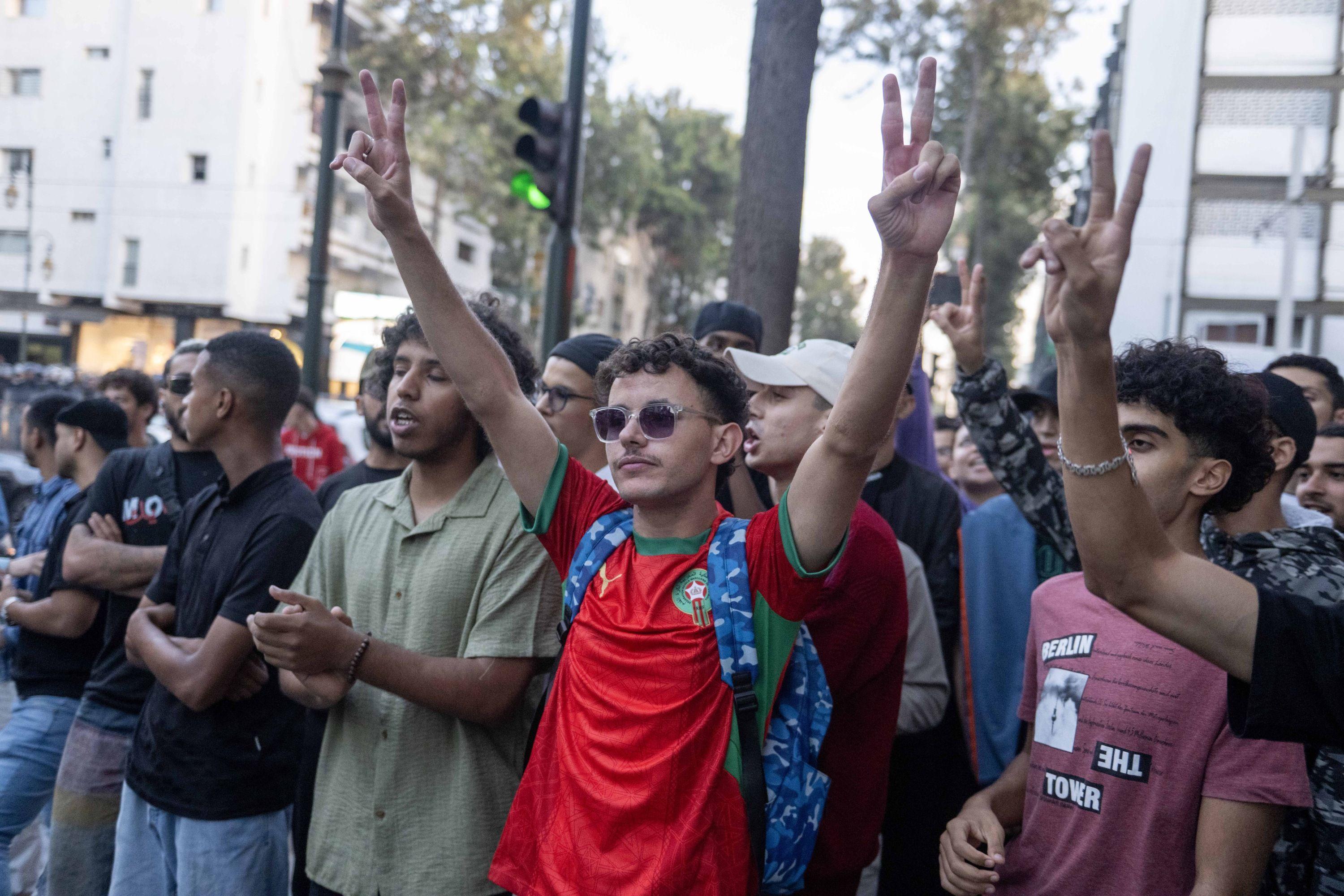 Jóvenes protestan en Rabat, Marruecos. En el centro de la imagen destaca un muchacho con camiseta roja, gafas de sol y los brazos en alto.
