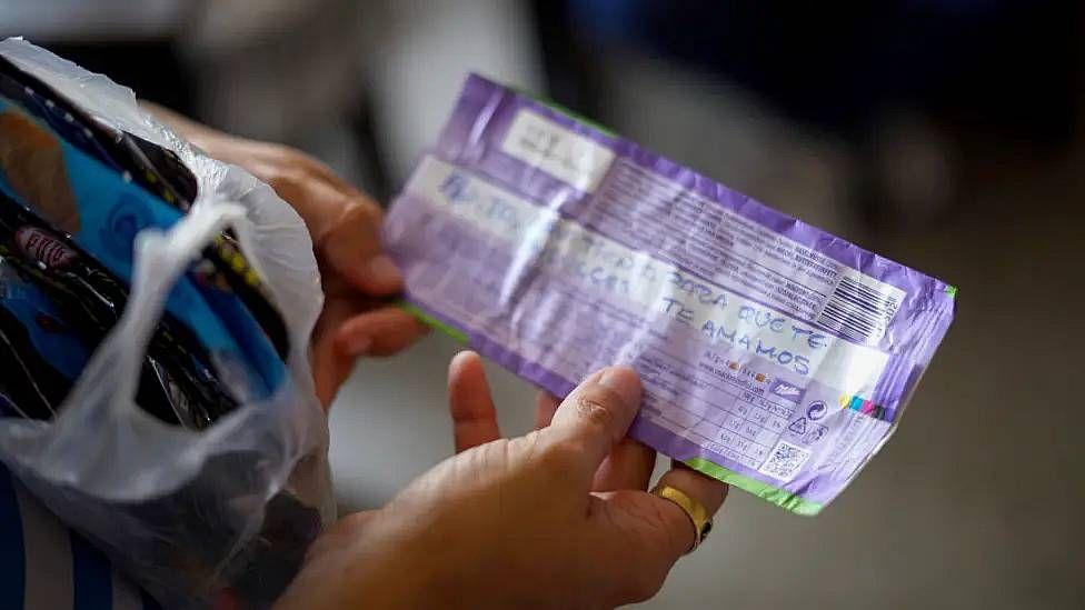 La esposa de Ángel Godoy, Adriana Briceño, sostiene un envoltorio con un mensaje escrito en tinta azul que dice "Papito, aquí tienes para que te endulces. Te amamos".