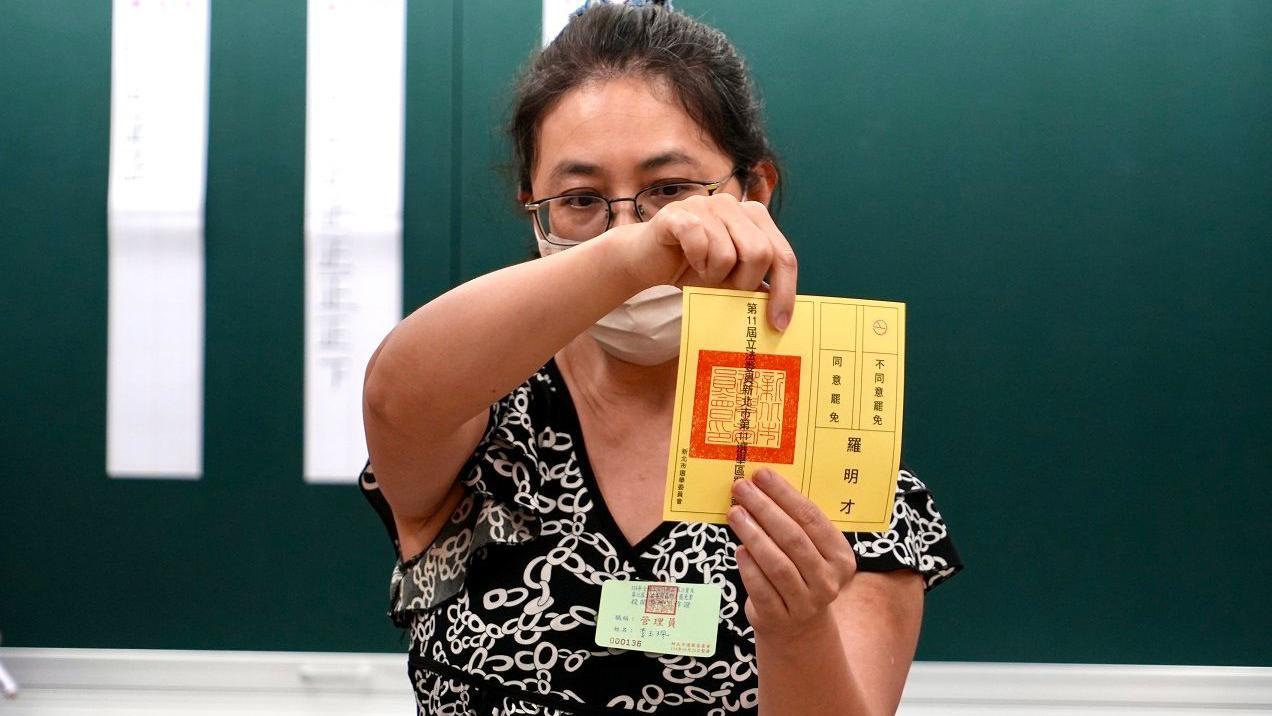 一名女士雙手持有一張黃色選票，向前展示。