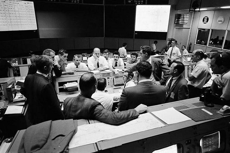 Reuni&atilde;o na sala de controle da miss&atilde;o Apollo 13, com as pessoas com apar&ecirc;ncia preocupada, tentando encontrar solu&ccedil;&otilde;es para trazer a espa&ccedil;onave defeituosa de volta &agrave; Terra