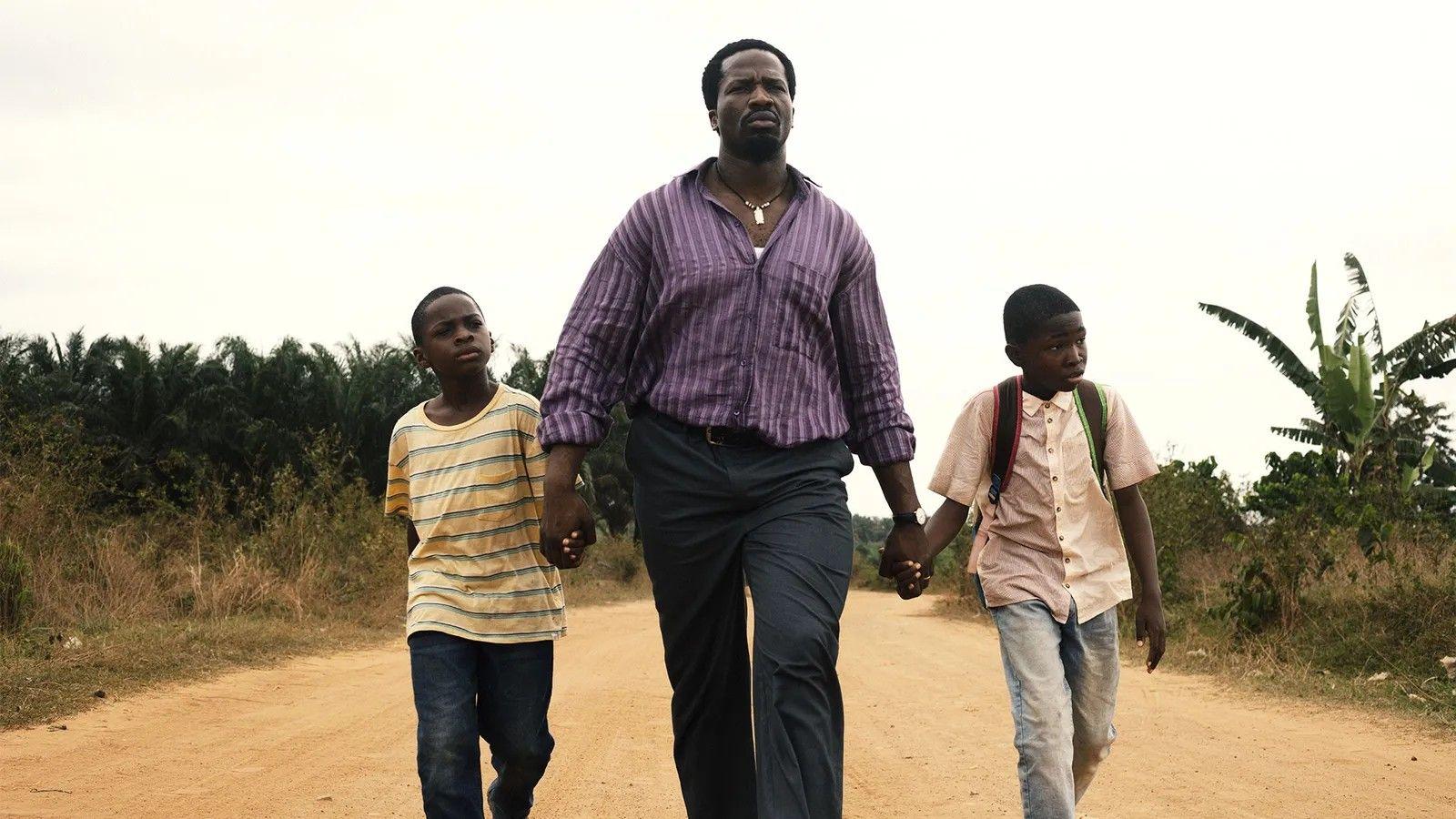 Homem caminhando em rua de terra de mãos dadas com os dois filhos