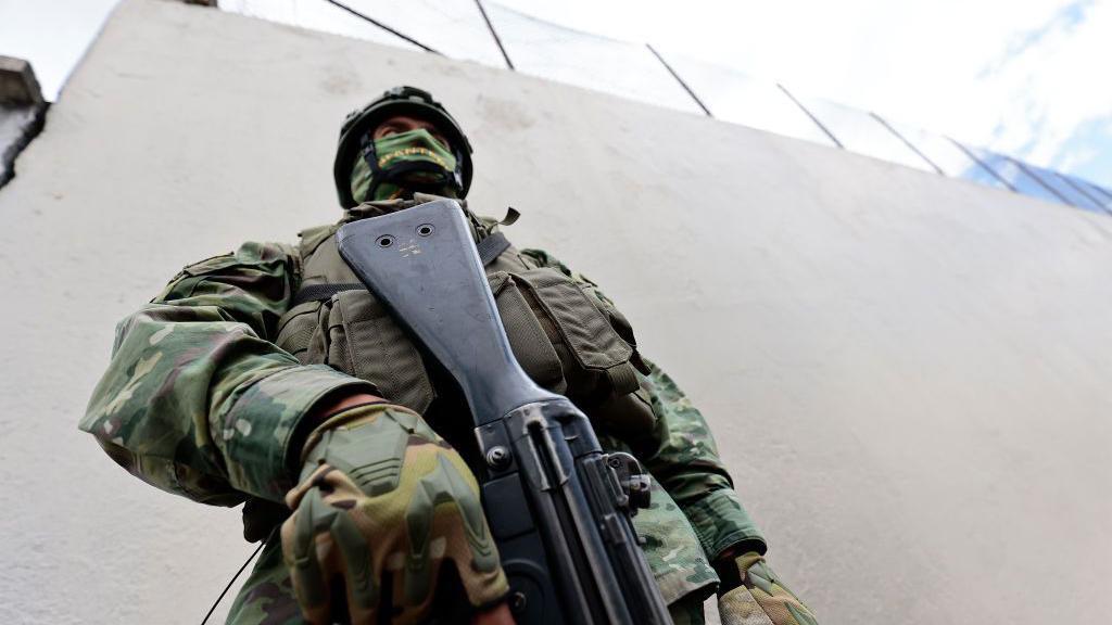 Un soldado con la cara cubierta y casco sostiene un fusil.