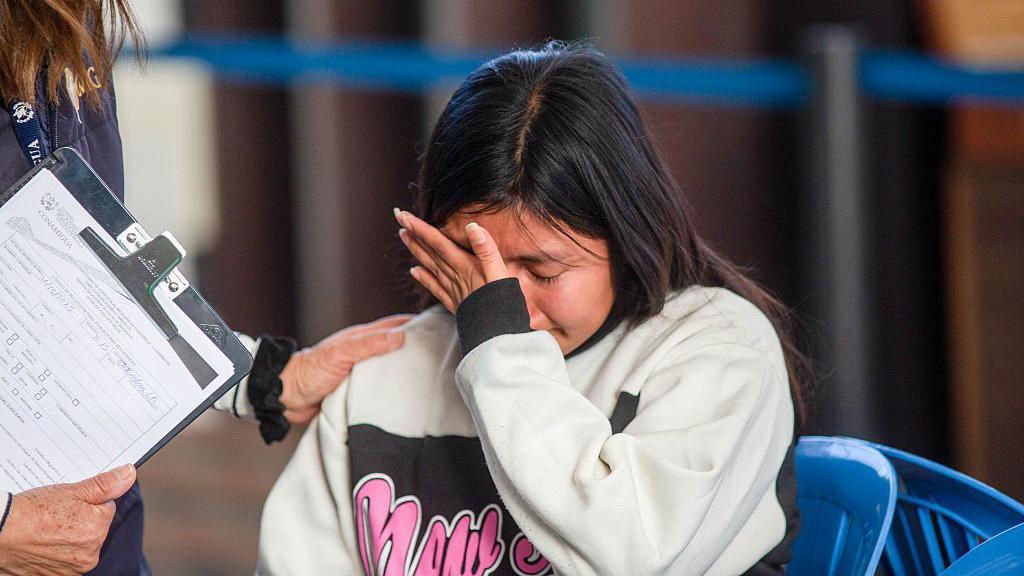 Una mujer guatemalteca deportada llora mientras habla con un agente del Instituto Guatemalteco de Migración en el centro de inmigración, tras llegar al Aeropuerto Internacional La Aurora luego de su deportación desde los Estados Unidos.
