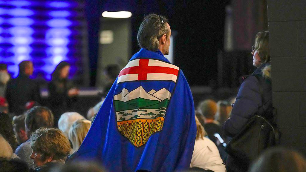 Un adepto lleva una bandera de Alberta colgada a la espalda mientras se pone de pie durante un evento en el Ayuntamiento de Independencia de Alberta en Calgary, Alberta, Canadá