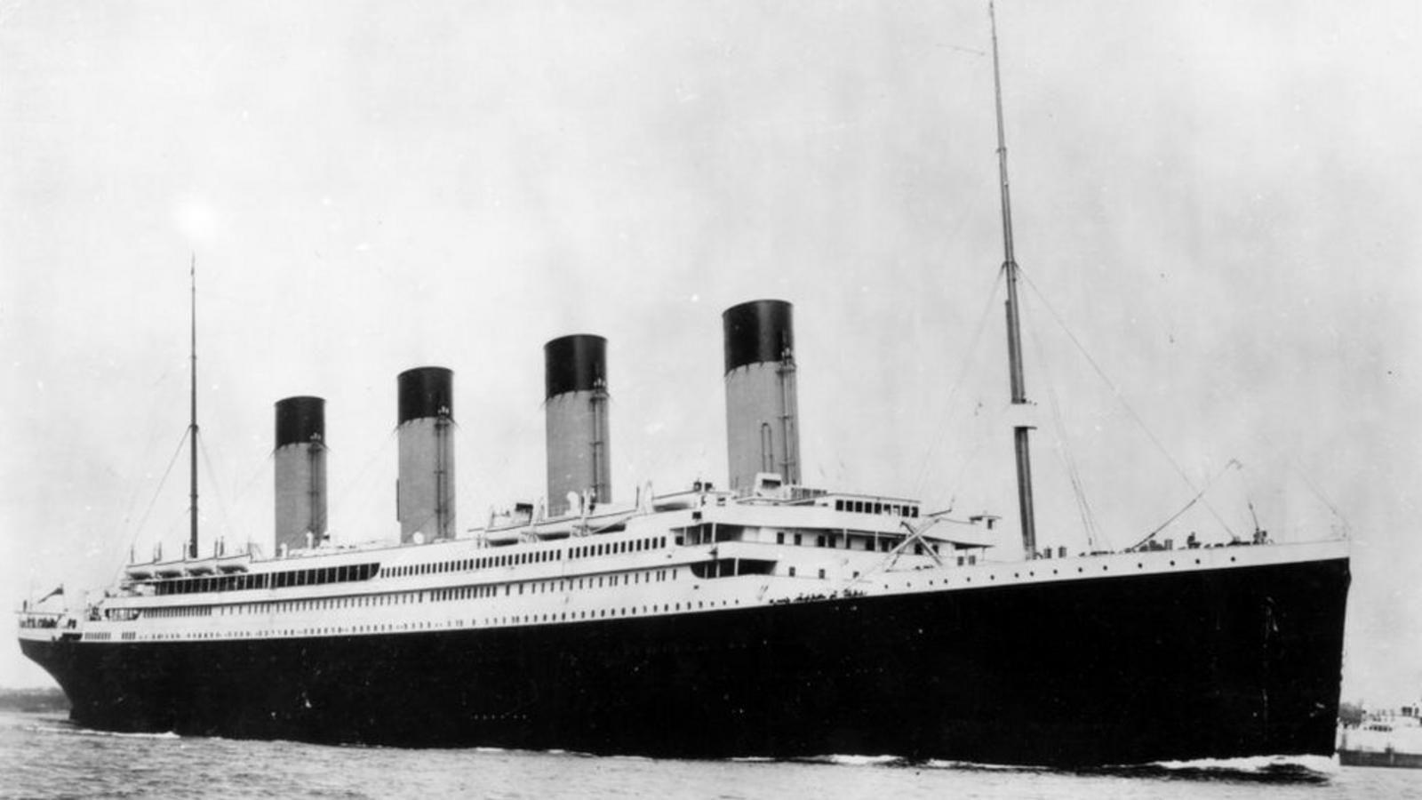 Imagen en blanco y negro del Titanic navegando muestra el estribor de la nave con sus cuatro gigantescas chimeneas y dos grandes hastas una en la proa y la otra en la popa