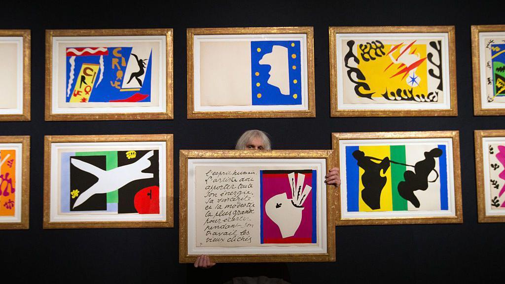 Una mujer sostiene una ilustración cerca de una colección de grabados originales de Henri Matisse de su portafolio de jazz en la casa de subastas Christie's el 17 de febrero de 2016 en Londres, Inglaterra