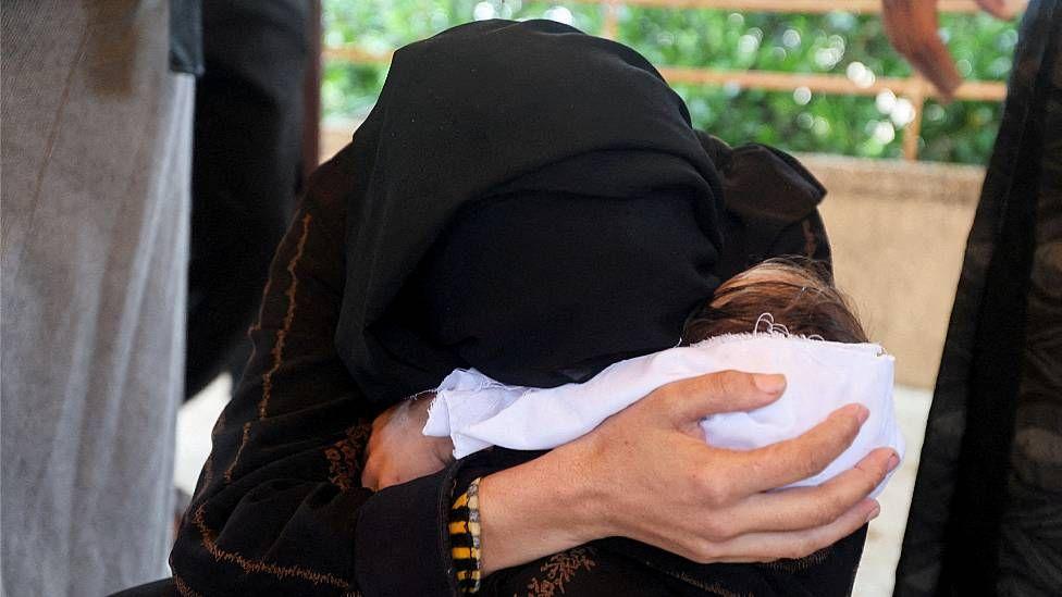 La madre de la bebé Rahaf Abu Jazar abraza a su hija que está envuelta en una sábana blanca.