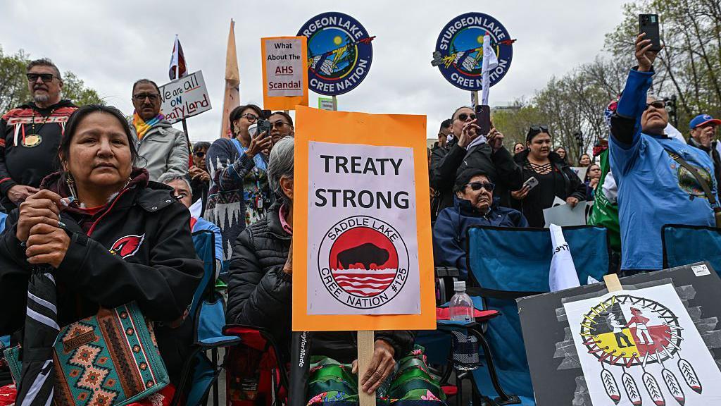 Una imagen que muestra a decenas de miembros de las Primeras Naciones reunidos frente a la legislatura de Alberta en Edmonton, sosteniendo carteles que dicen FIRME CON EL TRATADO y TODOS VIVIMOS EN TIERRA BAJO TRATADO