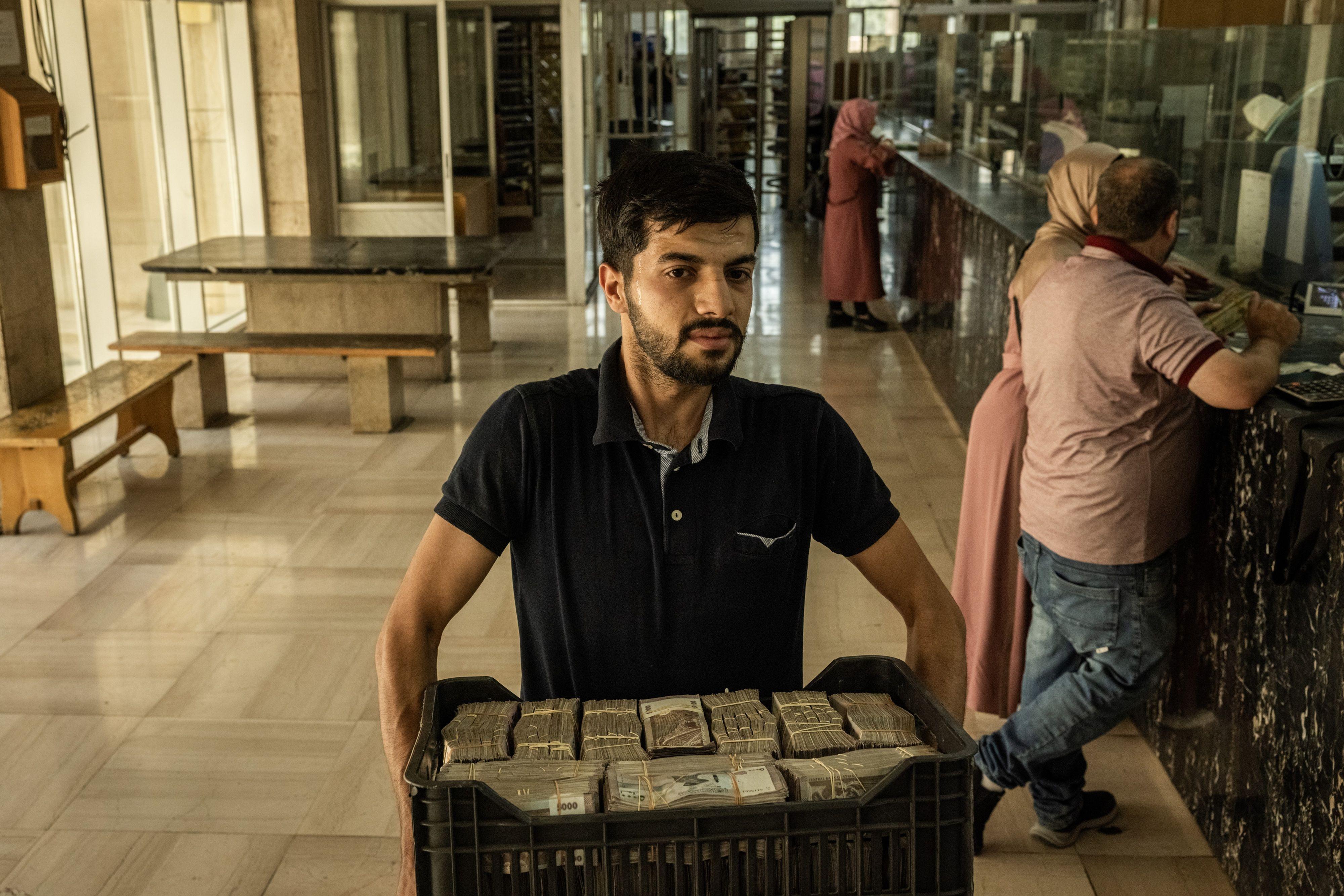 موظف يحمل صندوقاً مليئاً بالأوراق النقدية من فئة 5000 ليرة سوريا في المصرف المركزي السوري في 17 يونيو/حزيران 2025
