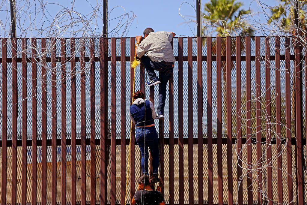 Migrantes intentan trepar la barrera fronteriza desde Mexicali, México hacia Calexico, EE. UU., el 13 de mayo de 2023 en Mexicali, Baja California. +Gary Coronado / Los Angeles Times vía Getty Images)