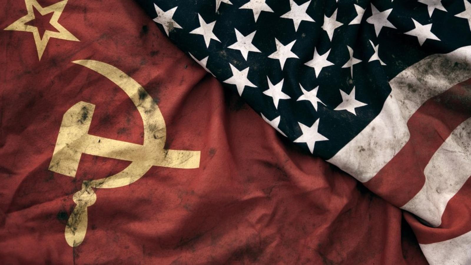 Imagen compuesta muestra una bandera doblada de estrellas blancas sobre un fondo azul y franjas rojas y blancas sobre otra bandera ligeramente arrugada de color rojo sólido con el símbolo amarillo de la hoz y el martillo y una estrella. Ambas banderas parecen estar manchadas con el humo dejado por explosiones