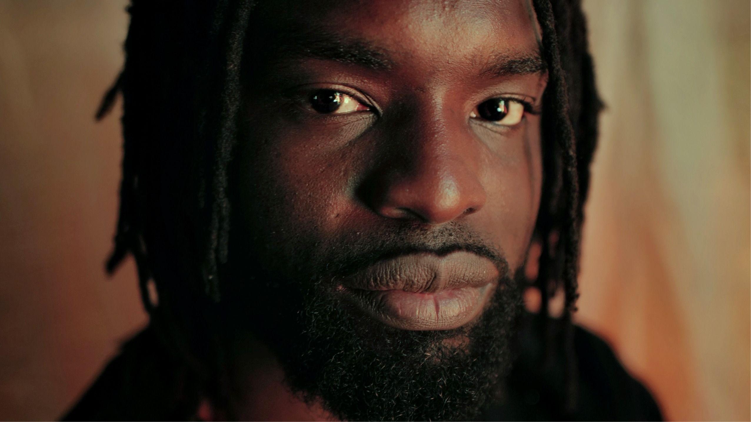 Un primer plano de Meji Alabi, con barba y rastas, mirando a la cámara