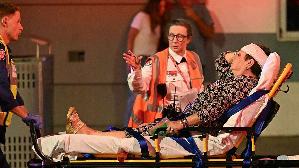 Uma mulher com uma bandagem na cabeça é transportada em uma maca.
