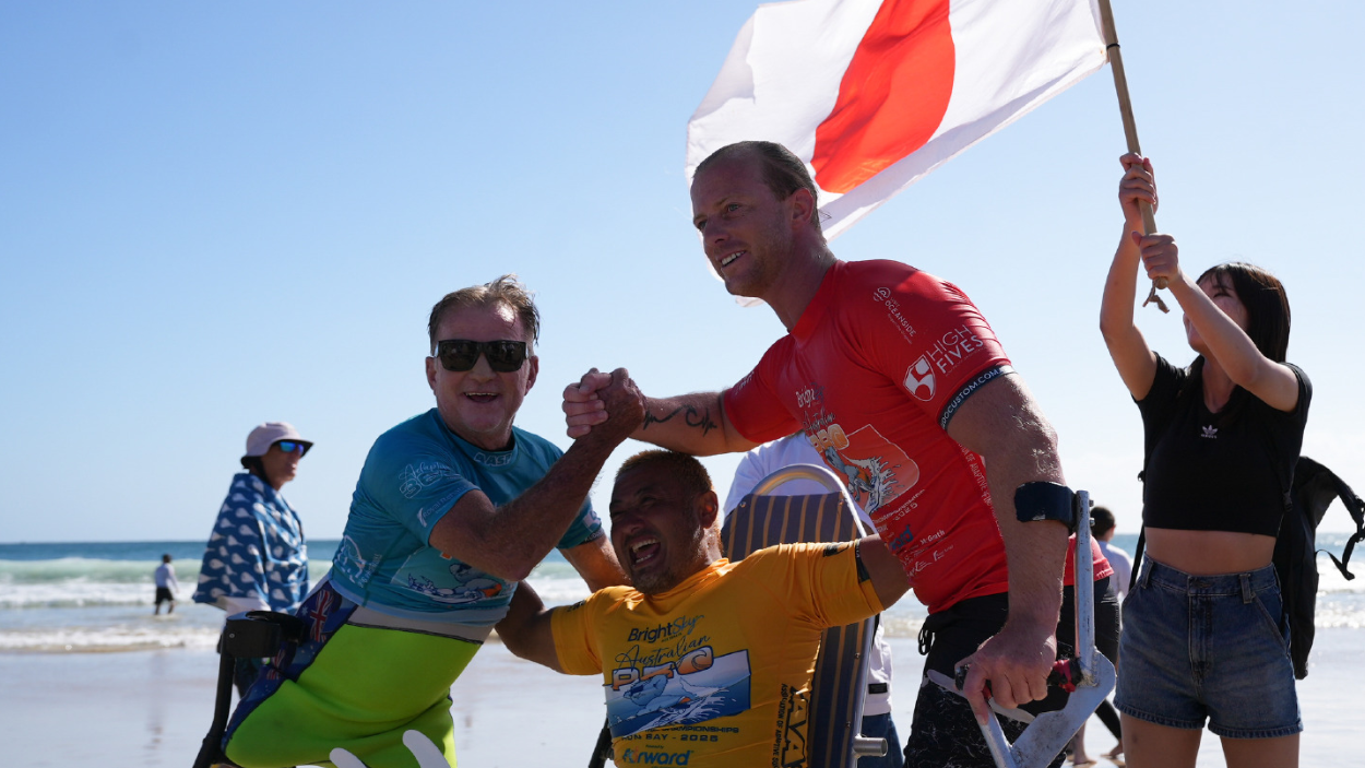 Em clima de comemora&ccedil;&atilde;o, Llywelyn Williams e outros dois surfistas posam para uma foto ap&oacute;s a competi&ccedil;&atilde;o, com o mar ao fundo
