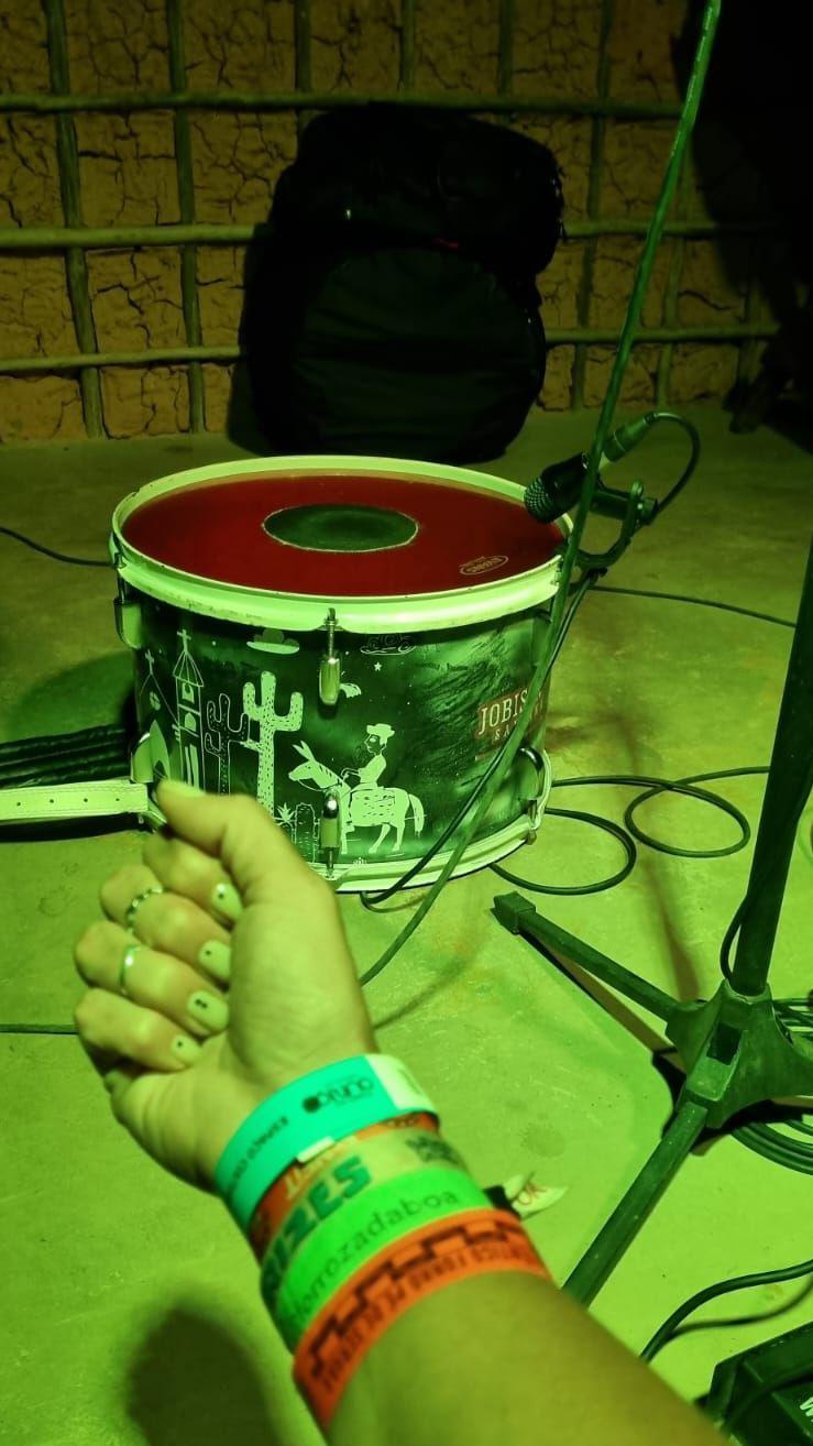 Bra&ccedil;o de Priscila com diversas pulseirinhas de festivais de forr&oacute;, com uma zabumba e uma parede de taipa ao fundo