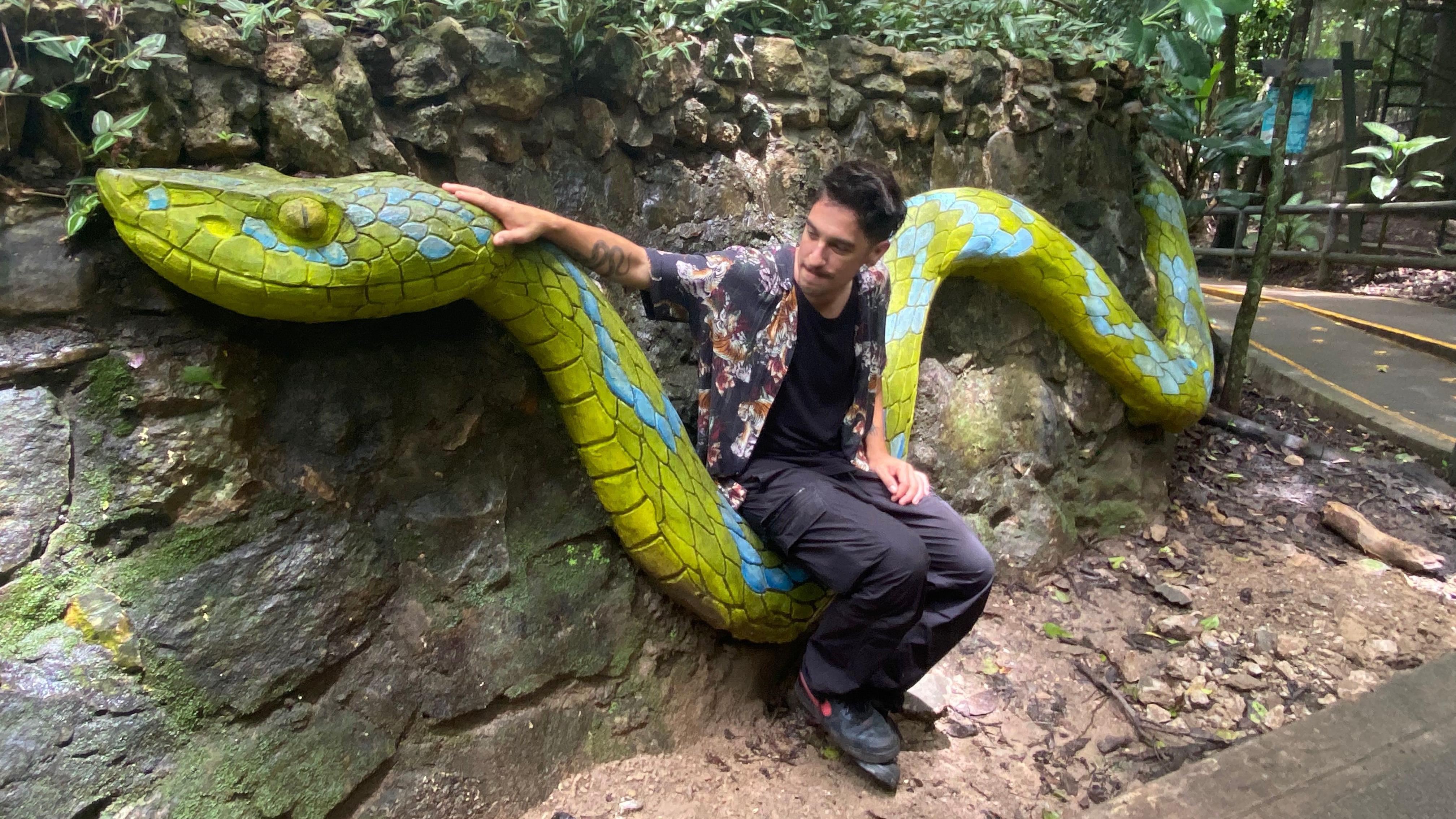 Andrés Cota Hiriart sentado en una serpiente verde y azul de cemento.