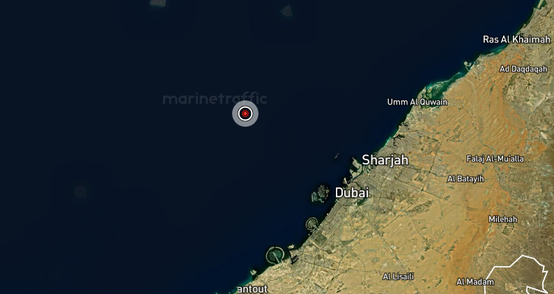 A imagem mostra um mapa de sat&eacute;lite da costa dos Emirados &Aacute;rabes Unidos, com destaque para cidades como Dubai, Sharjah e Ras Al Khaimah &agrave; direita, em tons de areia contrastando com o azul escuro do Golfo P&eacute;rsico &agrave; esquerda. No mar, um ponto marcado com um alvo vermelho indica a localiza&ccedil;&atilde;o de um navio, com a marca d&rsquo;&aacute;gua &ldquo;MarineTraffic&rdquo; vis&iacute;vel ao fundo.