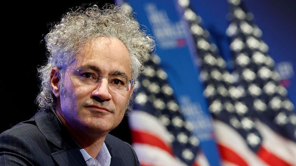 Alex Karp, com bandeiras americanas desfocadas ao fundo