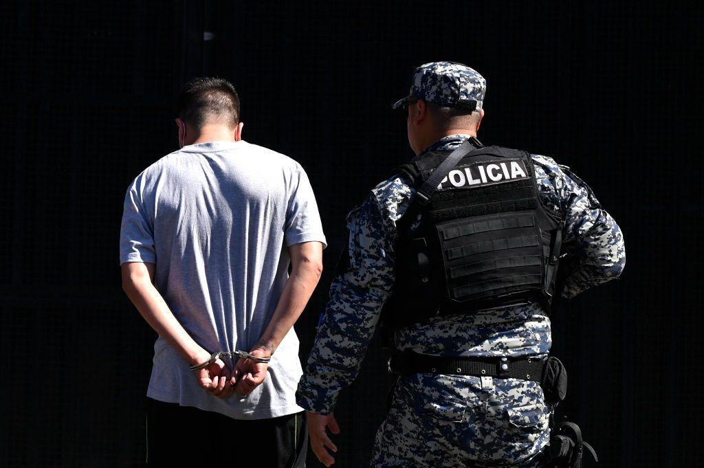 Un hombre arrestado por supuestos vínculos con pandillas es escoltado por un oficial de la Policía Nacional Civil durante el estado de emergencia declarado por el gobierno salvadoreño en el centro penal de San Salvador, el 22 de junio de 2022. (Foto de MARVIN RECINOS / AFP) (Foto de MARVIN RECINOS/AFP a través de Getty Images)